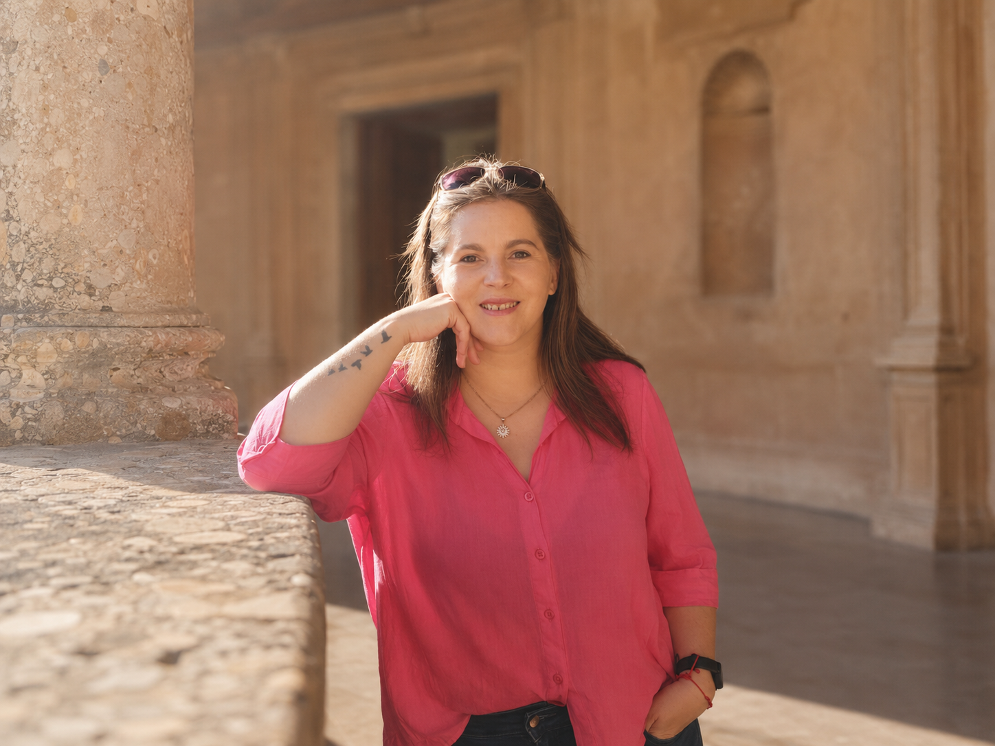 Eli Tarasiuk con camisa rosa apoyada en la arquitectura de piedra de la Alhambra